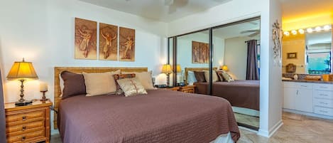 A bedroom with a large bed, two bedside tables with lamps, a ceiling fan, and artwork on the wall.