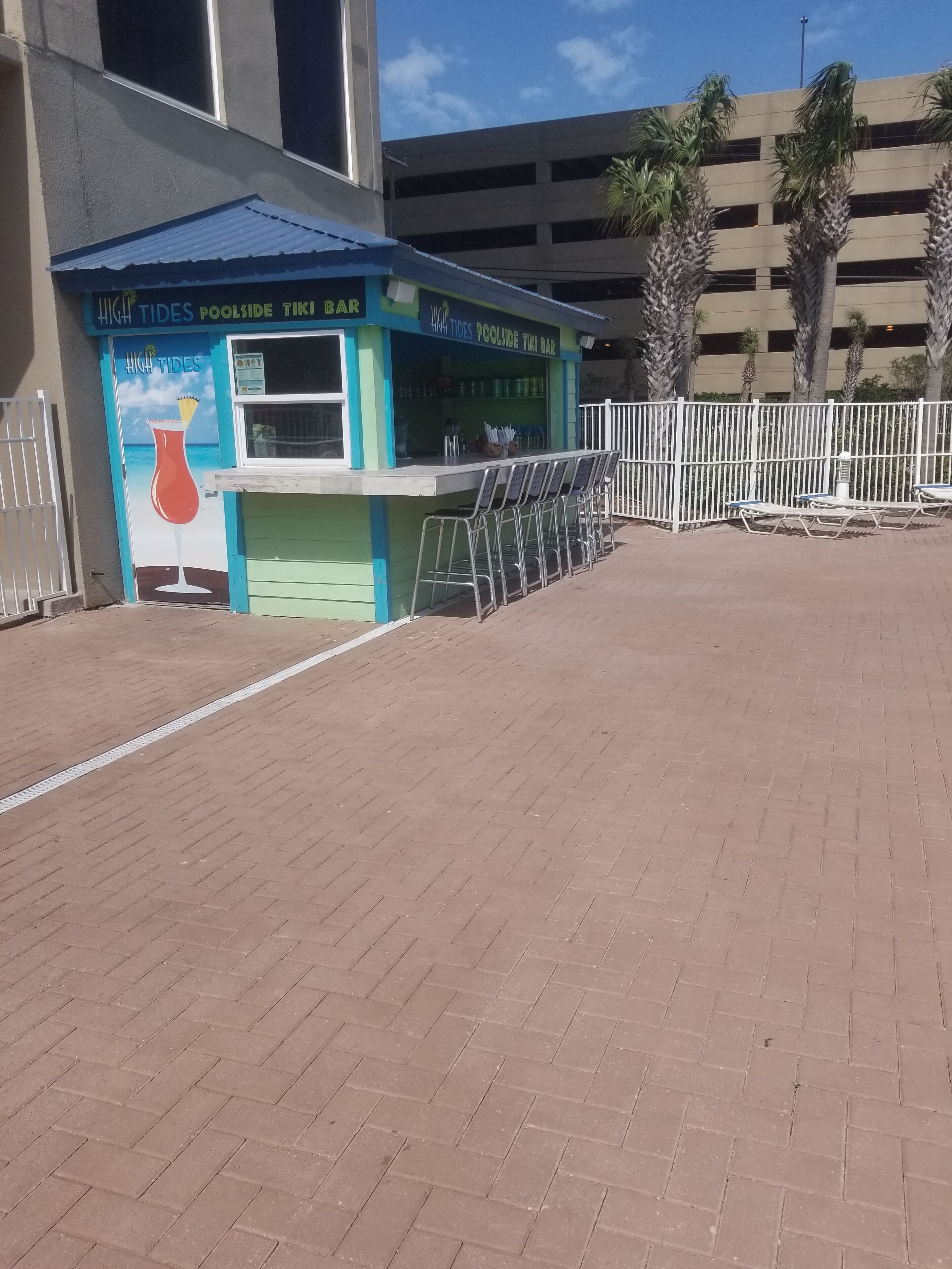 A tiki bar named 'High Tides Poolside Tiki Bar' with outdoor seating and a beach-themed mural.