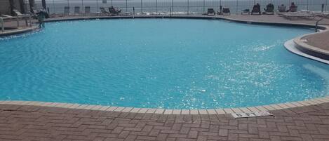 Una piscina con plataforma de ladrillo, valla metálica y vista al océano.