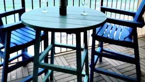 Una mesa redonda con dos sillas y una botella de vino en un balcón con vistas al océano.