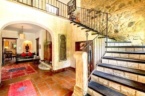 Un intérieur spacieux avec un escalier menant à un niveau supérieur, un coin salon confortable avec un canapé et des coussins, et un élément décoratif mural.