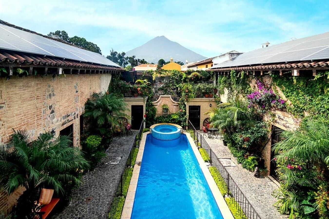 A swimming pool surrounded by lush greenery and buildings with terracotta roofs.