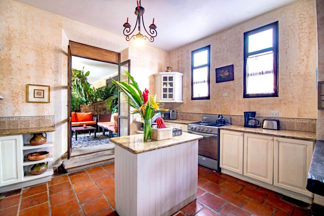 Una cocina con una isla central, armarios blancos, estufa y cafetera.
