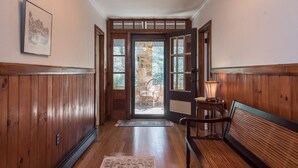 A hallway with wooden paneling, a bench, a rug, and a door leading to an outdoor area with a chair and a lamp.