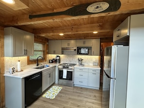 A cabin kitchen with wooden ceiling, white cabinets, stainless steel appliances, and a welcome sign.