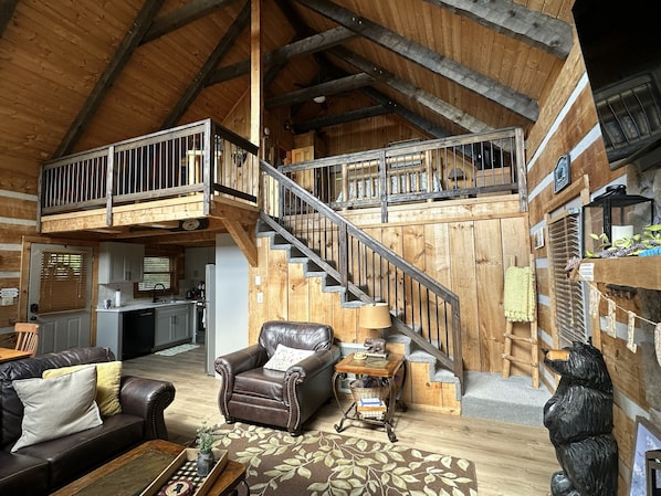 A rustic cabin interior with a loft bedroom, a dining area, and a kitchen.