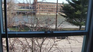 Vista per una finestra amb branques despullades en primer pla, un edifici amb múltiples finestres al fons i un cel serè.