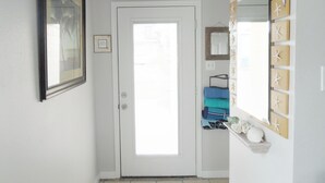 A hallway with a white door, a framed picture on the left, and a mirror with starfish decorations on the right. - Tarpon Qtrs! 1BR/1BA w/Dog Friendly Fenced Yard, Walk to the Beach! (Port Aransas)