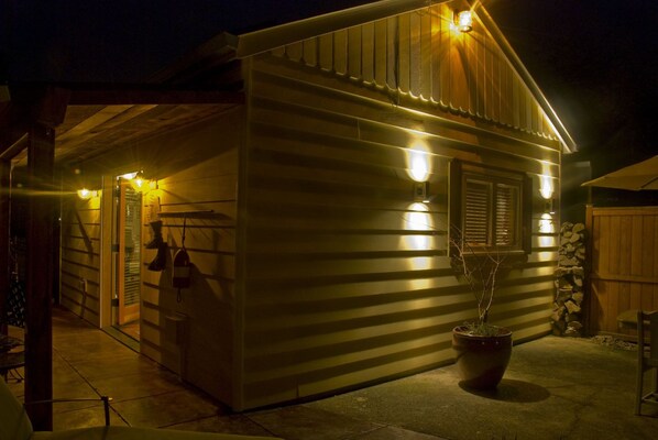 Une cabane en bois avec une véranda, une plante en pot et un mur en pierre.