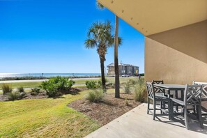 Un patio con mobiliario exterior, vista al océano y un edificio al fondo.