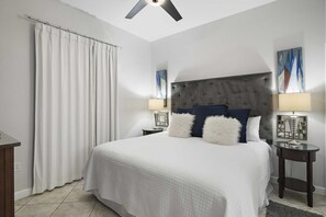 Habitación de hotel con una cama grande, dos mesitas de noche con lámparas, un ventilador de techo y vistas a la ciudad.