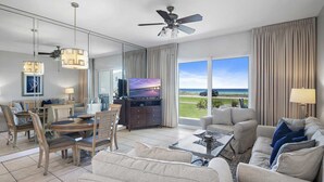 A spacious living room with a large flat-screen TV, a ceiling fan, and a view of the ocean. - Beach Retreat 105 Beach service in Season  Destin Pet Friendly (Destin)