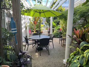 Relax in the serene outdoor patio area with a round table and four chairs, surrounded by lush greenery and a large umbrella.