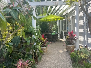 A covered patio area with a table and chairs, surrounded by potted plants and a pergola.