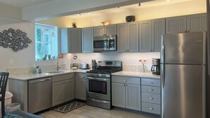 A modern kitchen with grey cabinets, stainless steel appliances, and a marble countertop.