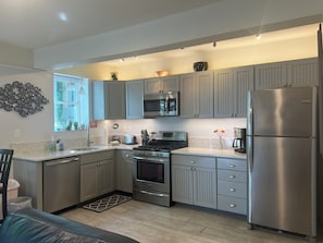 A modern kitchen with grey cabinets, stainless steel appliances, and a marble countertop.
