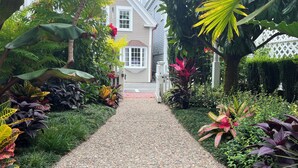 A pathway leading to a house surrounded by lush greenery and various plants.