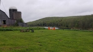 Paisaje rural con un granero, un silo y un área de picnic con sillas anaranjadas.