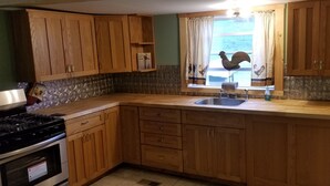 Una cocina con armarios de madera, un lavamanos de acero inoxidable y una ventana con cortinas.