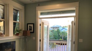 En stue med fjernsyn, gulvlampe og sofa. Der er en skydedør, der fører ud til en balkon med udsigt over huse og træer.