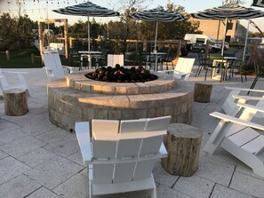 Uteservering med en eldstad, omgiven av stolar och bord, under randiga parasoller.