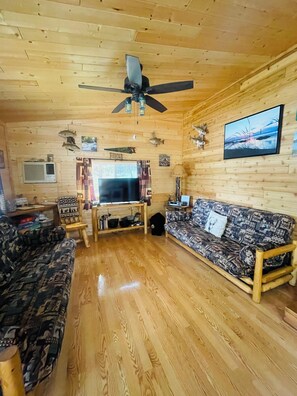 A wooden interior with a ceiling fan, a television, a sofa, and a patterned rug. - Lakefront Cabin, Pet Friendly, WIFI , near Pictured Rocks Munising Mi. (Wetmore)