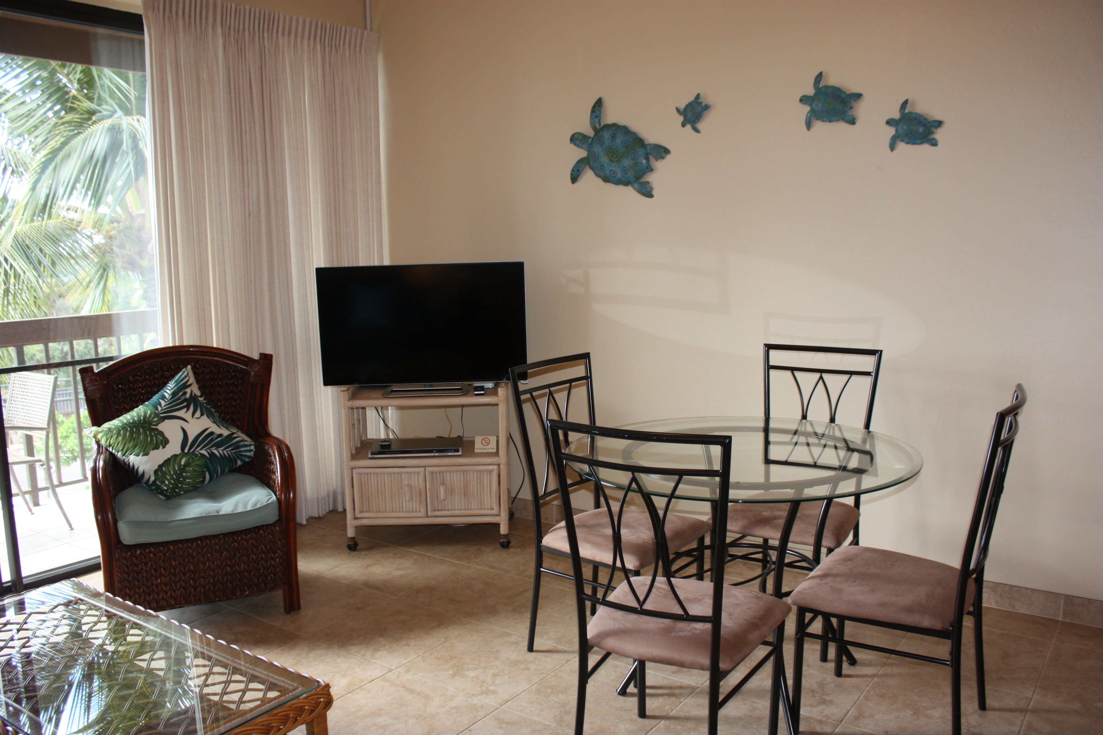 A living room with a TV, a glass table, and four chairs.
