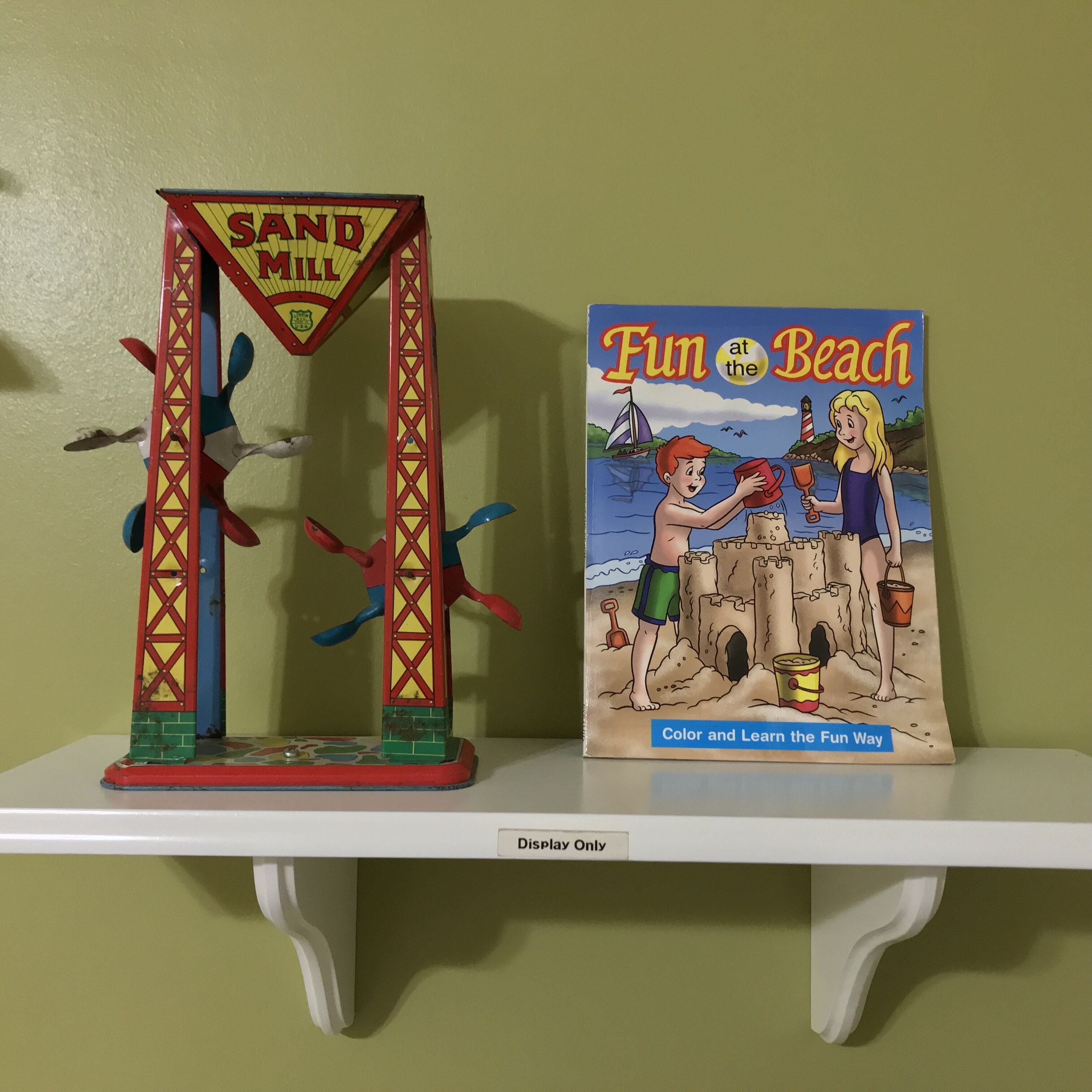 A sand mill and a children's book titled "Fun at the Beach" on a shelf.