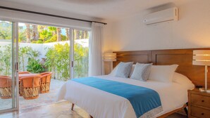 A hotel room with a large bed, a wooden headboard, a nightstand, and a sliding glass door leading to an outdoor area with a table and chairs. - Villa Luna Nueva - Concierge and Maid Service included (Cabo San Lucas)