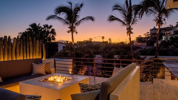 A rooftop terrace with a fire pit, seating area, and a view of palm trees and buildings at sunset. - Villa Luna Nueva - Concierge and Maid Service included (Cabo San Lucas)