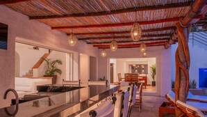 A modern kitchen with a marble countertop and a built-in sink. There is a dining area with wooden chairs and a table. - Villa Luna Nueva - Concierge and Maid Service included (Cabo San Lucas)