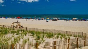 A beach with a wooden fence, beach umbrellas, and people relaxing.