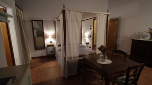 Un dormitorio con una cama con dosel, una mesita de noche con lámpara y una mesa de comedor de madera con sillas.