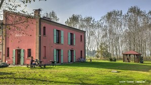Un edificio rosa con contraventanas verdes, un pabellón y una mesa de picnic en un área con césped.