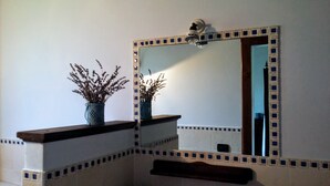 Un baño con espejo, dos jarrones con plantas secas y un revoque de azulejos.