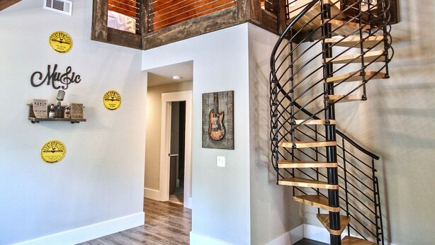 Una habitación amplia con techo de madera, una escalera de caracol y un muro decorado con motivos musicales.