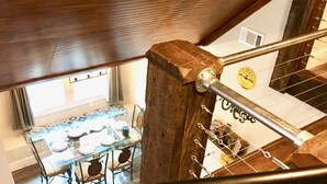 Una escalera de madera con barandilla de metal que lleva a un comedor con una mesa preparada para cuatro personas y sillas.