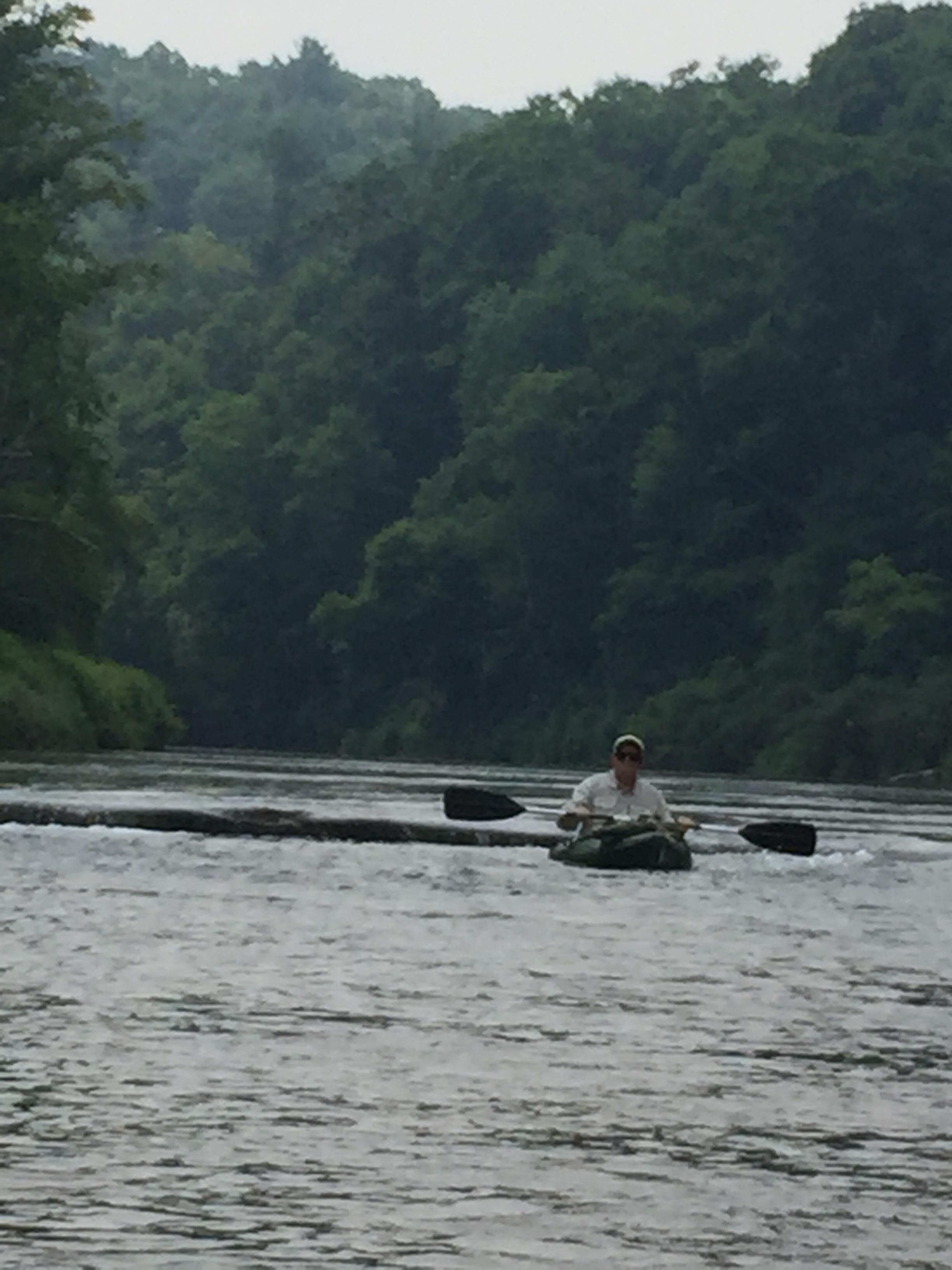 Una persona remando un kayak en un río rodeado de un bosque frondoso.