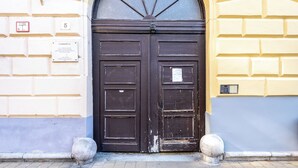 A double wooden door with a black frame, set within a stone archway, flanked by two stone bollards. - Large 3BR/3BA Flat Next to Central Market | Free Parking (Budapest)