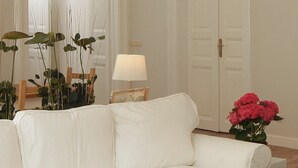 A white leather sofa in a room with a wooden floor, a white lamp, and a vase of pink flowers. - Large 3BR/3BA Flat Next to Central Market | Free Parking (Budapest)