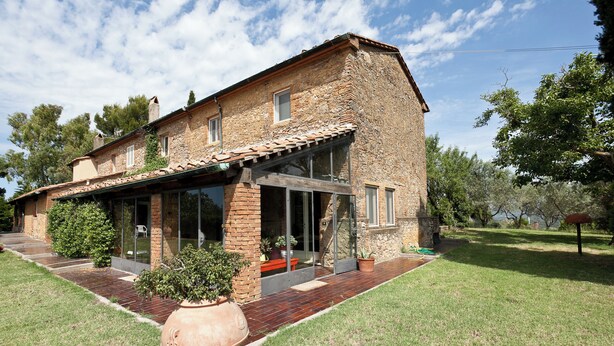 Una casa de piedra con techo de tejas, ventanas amplias y un patio empedrado.