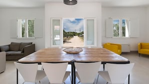 Comedor con mesa de madera, sillas blancas y vista a un sendero que lleva a un paisaje natural.