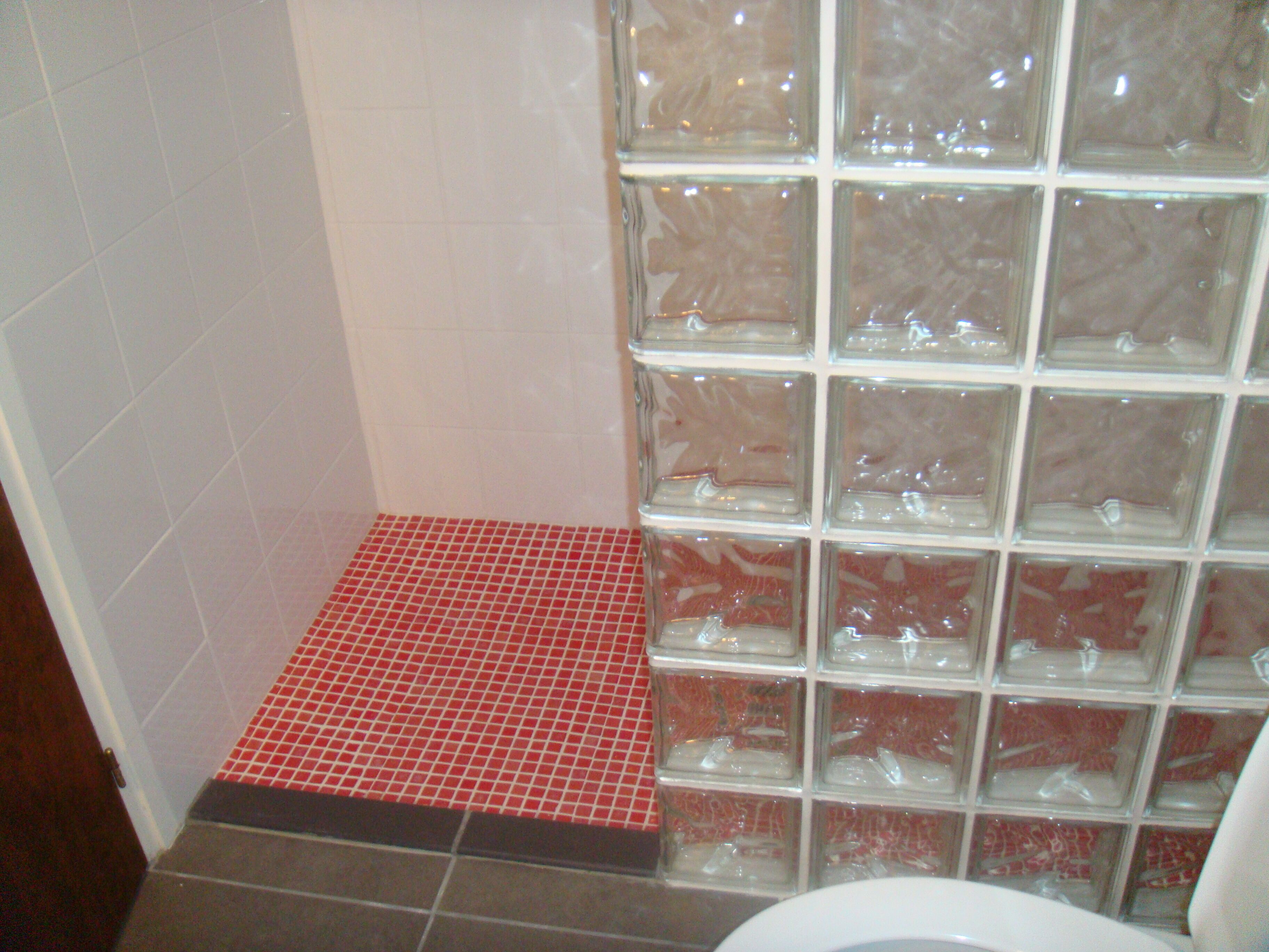 A bathroom with a tiled floor, a glass shower enclosure, and a white toilet.