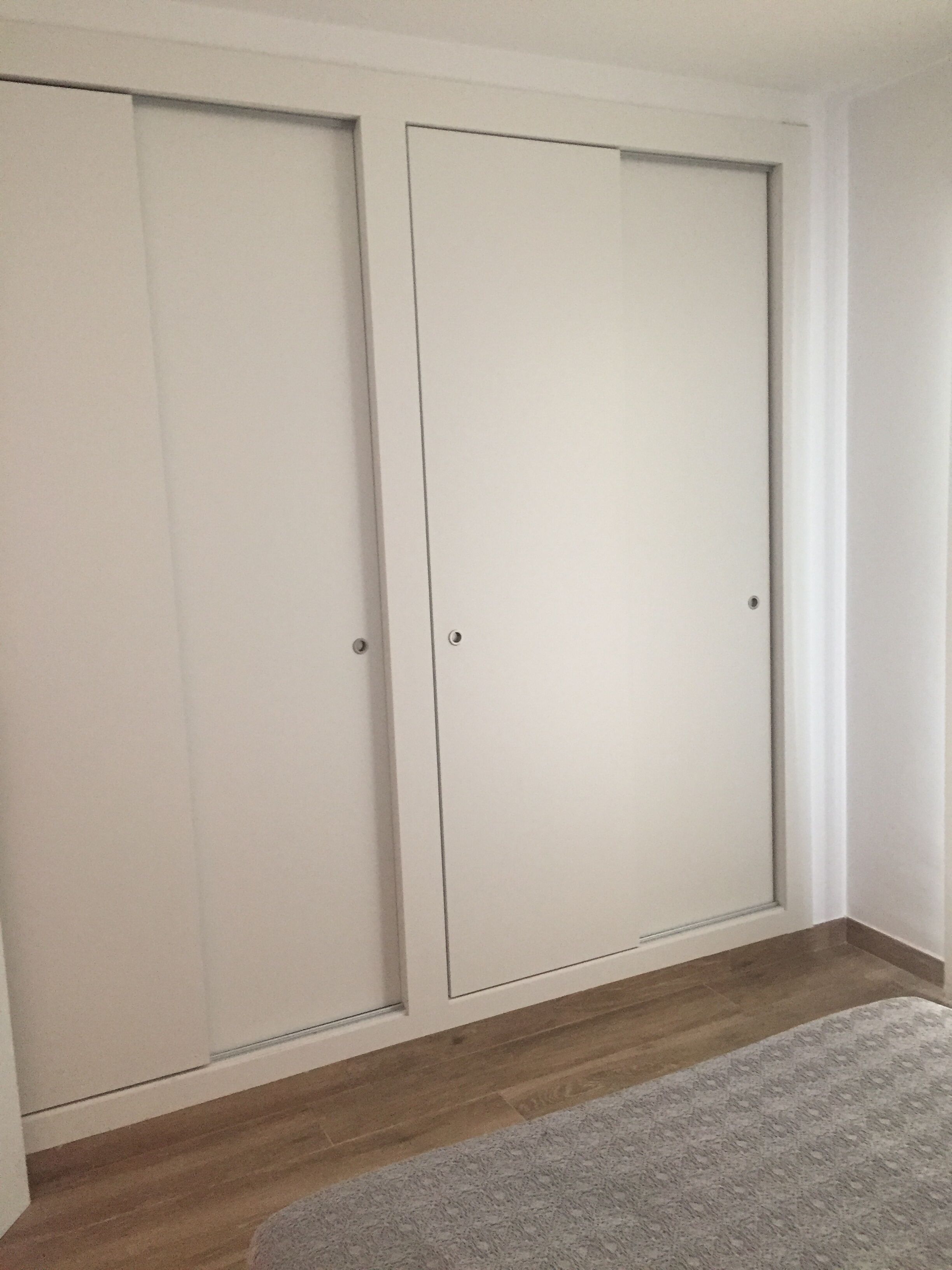 A room with a large white wardrobe, a wooden floor, and a grey rug.