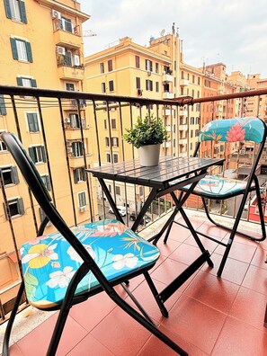 A balcony with a table and two chairs, a potted plant, and a view of multi-story buildings. - NEW and colored flat ,10 minutes from Ancient Rome (Roma)