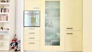 Een kitchenette met een inbouwoven, een koelkast en een plank met boeken.