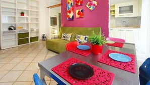 Een moderne woonkamer met een eethoek, met een bank, een eettafel met rode placemats en een levendige roze accentmuur.
