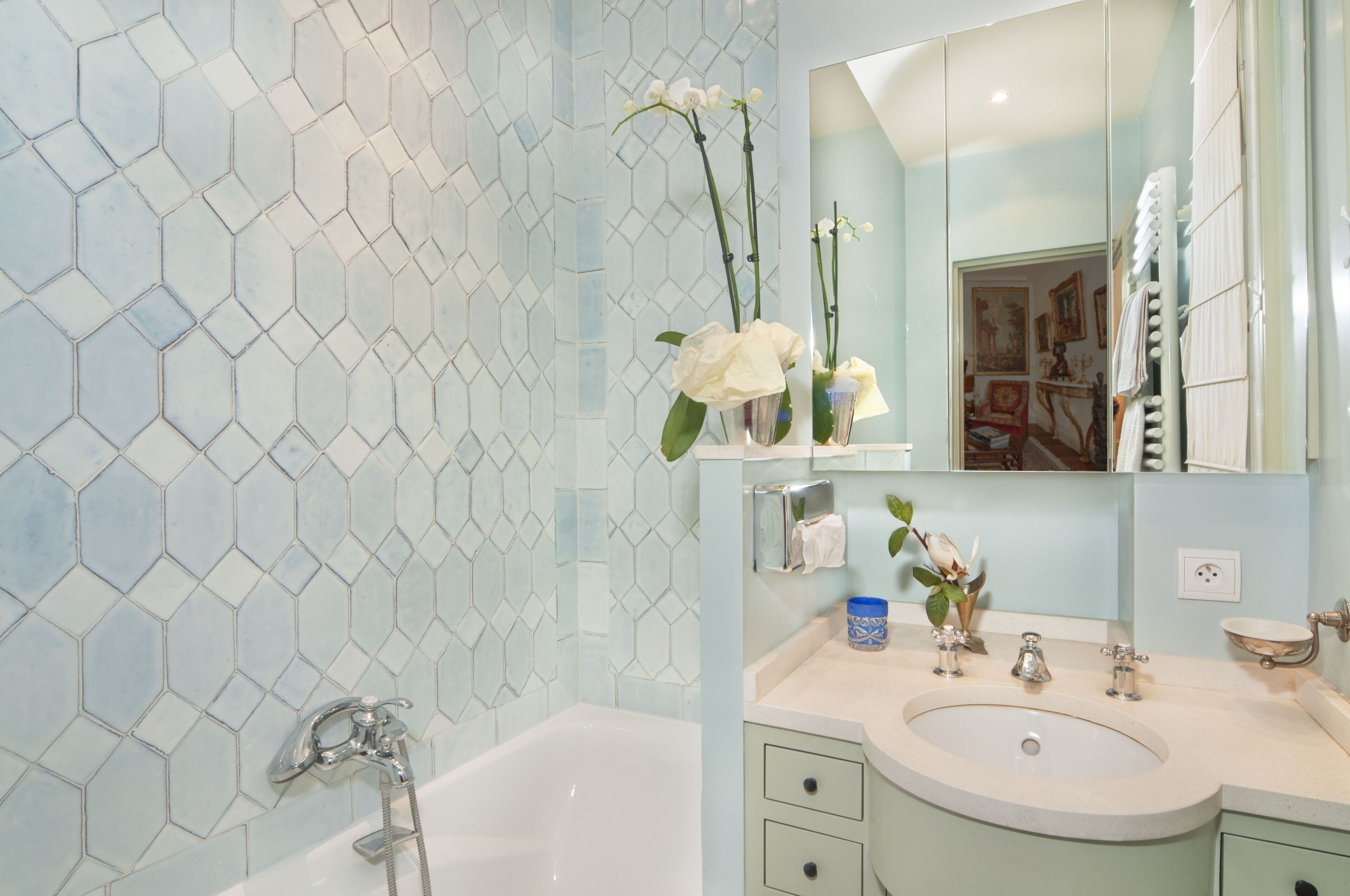 A bathroom with a hexagonal tile backsplash, a bathtub, a vanity with a sink, and a mirror.
