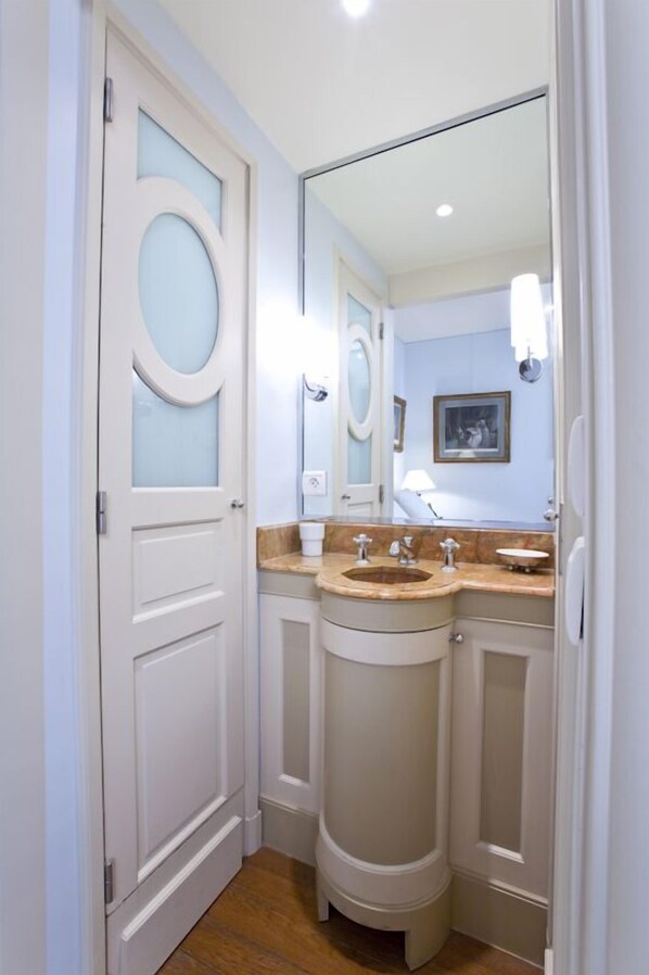 Une petite salle de bain avec une porte blanche, un grand miroir et un lavabo équipé de deux robinets.