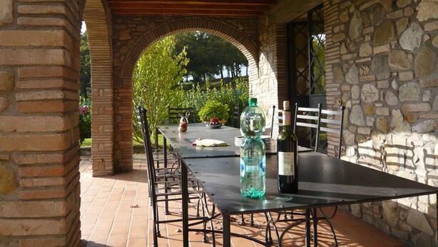 Une terrasse extérieure avec une table et des chaises, un mur en pierre et une vue sur la verdure.